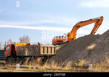 Il grande escavatore sta riempiendo dumper con terreno in cantiere, progetto in corso. Escavatore per macchine da costruzione a terrapieni. Foto Stock