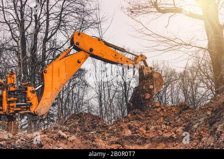 Un vecchio escavatore giallo nel mezzo della foresta scava una fossa della siviera per raccogliere l'acqua. Foto Stock