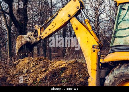Lavoratore e vecchio escavatore giallo nella foresta scavare una fossa per la raccolta di acqua. Foto Stock