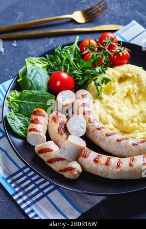 Pasto semplice aligot francese di patate schiacciato con formaggio fuso servito con salsicce, insalata fresca di spinaci, pomodori e foglie di insalata servito su un nero Foto Stock