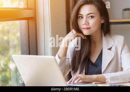 Business startup in Asia concept. Focalizzato giovane donna business asiatico con pensare faccia lavorare con il laptop sul posto di lavoro guardando la fotocamera, film in effetto Foto Stock