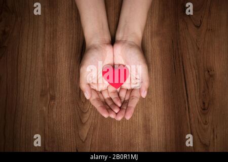 mani femminili che tengono il cuore rosso. giorno di san valentino, cura di salute, concetto di donazione, giorno di cuore del mondo. Foto Stock