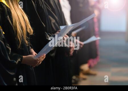 Coro cantanti holding partitura musicale e il canto per studenti il giorno di graduazione in università, college diploma inizio Foto Stock