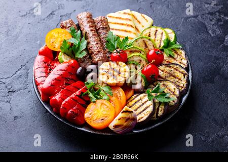 Spiedini di carne alla griglia e verdure su un piatto. Sfondo in pietra nera. Primo piano. Foto Stock