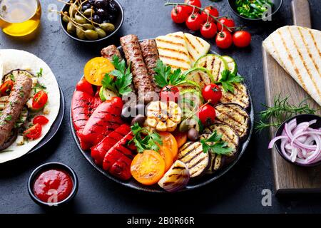 Spiedini di carne alla griglia, verdure su un piatto nero con tortillas, pane piatto. Ardesia pietra sfondo. Foto Stock