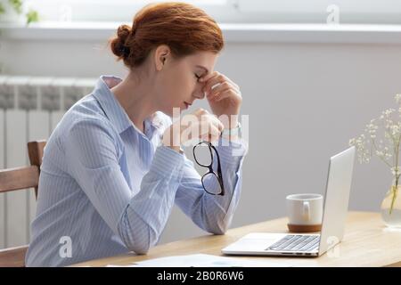 Donna d'affari stanca che prende gli occhiali, soffre dalla sindrome degli occhi asciutti dopo il lavoro lungo del calcolatore, impiegato sfinito seduto alla scrivania, naso massaggiante Foto Stock