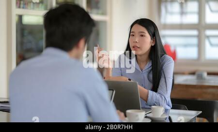 Scatto corto di due businesspeople che si siing l'uno di fronte all'altro mentre consultandosi sul loro lavoro con il laptop del calcolatore Foto Stock