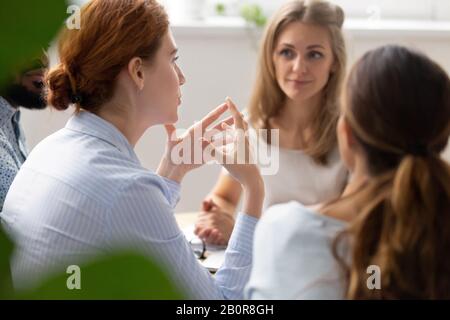 Donna d'affari con vista posteriore che discute il progetto con i colleghi diversi al briefing in sala riunioni, i dipendenti seduti insieme alla scrivania, condividendo i pensieri, ide Foto Stock