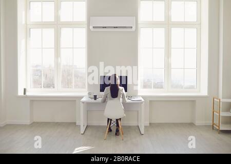 Il giovane accende il condizionatore d'aria raffredda l'aria mentre si siede sul divano nella stanza Foto Stock