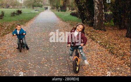 Giovani fratelli caucasici in bicicletta su una colorata strada del parco durante la vacanza autunnale Foto Stock