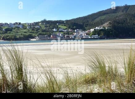 Piccolo villaggio di pescatori dalla spiaggia con erba sulle dune di sabbia. O Barqueiro o El Barquero, Galizia, Spagna. Foto Stock