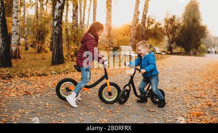 Adorabili ragazzi caucasici vestiti con jeans che cavalcano le biciclette nel parco in un autunno colorato giorno Foto Stock