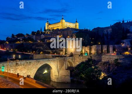 Porta del Ponte, Ponte dell'Alcantara, Puente del Alcantara, sul fiume Tajo, con Alcazar de Toledo, vista notturna, Toledo, Castilla-la Mancha, Spagna Foto Stock