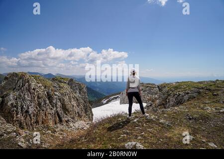 Una donna in grigio hoody in piedi girare la schiena su rocce di fronte al cielo sfondo Foto Stock