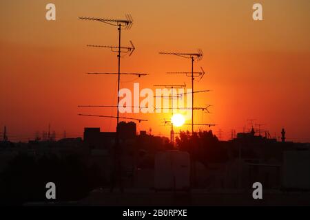 Antenne di ricezione televisiva analogica su un tetto dalla silhouette che si contrappone a un sole che tramonta Foto Stock