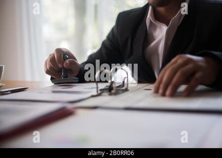 Manuale d'affari che preme il timbro di gomma approvato sul documento di contratto di affari Foto Stock