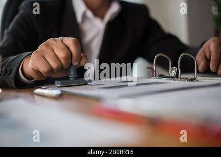 Manuale d'affari che preme il timbro di gomma approvato sul documento di contratto di affari Foto Stock