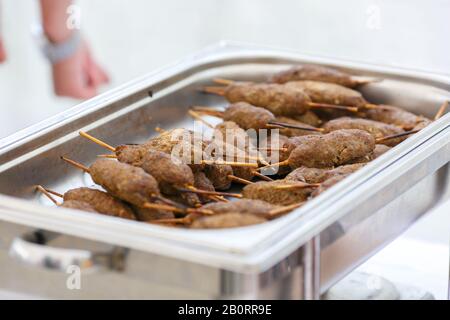 Un closeup di kebab grigliato saporito sui bastoni di legno nel contenitore di metallo Foto Stock