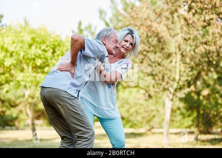 Donna aiuta un vecchio con mal di schiena nel parco Foto Stock