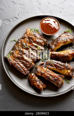 Grigliata di costine sulla piastra su pietra nera dello sfondo. Gustosi barbecue di carne. Foto Stock