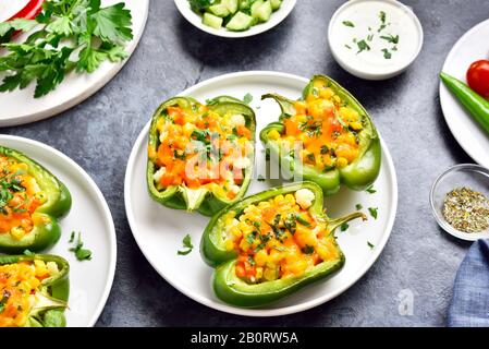 Peperoni verdi al forno riempiti di mais, carota, cavolfiore su piastra bianca su sfondo di pietra blu. Dieta sana o concetto di cibo vegetariano. Foto Stock