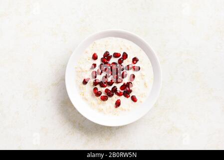 Melograno avena porridge in ciotola su sfondo di pietra chiaro con spazio libero di testo. Gustoso cibo sano per la colazione o il pranzo. Vista dall'alto, piatto Foto Stock