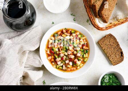 Tradizionale zuppa russa fredda Okroshka con salsiccia, verdure e kvass su sfondo di pietra chiara. Vista dall'alto, piatto Foto Stock