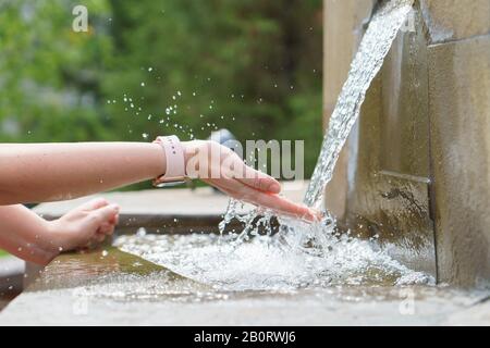 Un closeup di eleganti mani di donne con orologio, cattura il flusso d'acqua dalla fontana di pietra Foto Stock