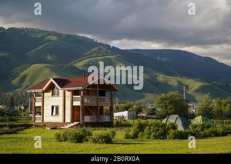 Prato verde con cottage turistico e tende turistiche, in campagna e foresta cresceva montagne sullo sfondo Foto Stock