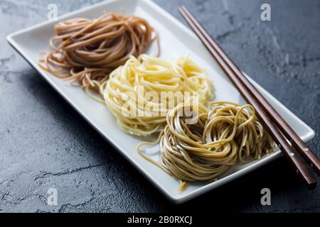 Varietà di tagliatelle di Soba su un piatto bianco. Cucina giapponese. Sfondo in ardesia nera. Primo piano. Foto Stock