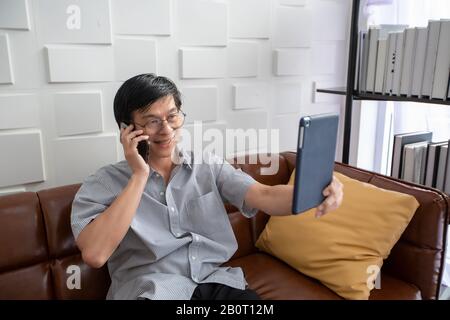 Uomo asiatico anziano che gioca tablet e video chiamata sul divano in soggiorno a casa ritratto di uomo anziano asiatico È Rilassante e felicità Con giocare ta Foto Stock