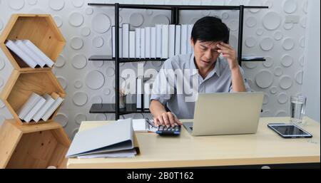 Un uomo asiatico anziano che usa il taccuino per lavorare e businesswoman serio circa il lavoro fatto fino al mal di testa Foto Stock