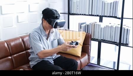 Uomo asiatico anziano che usa un tablet e un simulatore di realtà virtuale che gioca a giochi in salotto e si sente felice . Stile di vita concetto familiare senior a casa. Foto Stock