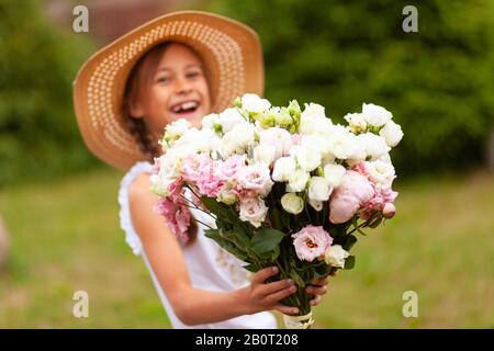 Ragazza con un bouquet di peonie bianche e rosa. Giornata estiva soleggiata. Ragazza in un cappello con orlo largo. Foto Stock