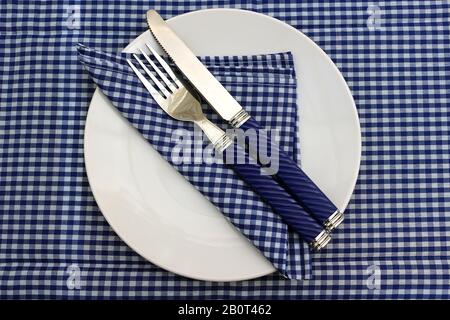 Una piastra bianca con tovagliolo e coltello e forchetta su un panno da tavolo blu gingham Foto Stock