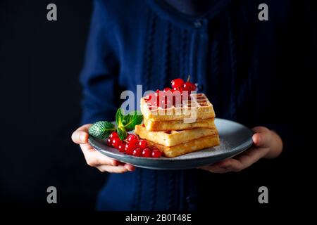 Mani di donna che tengono un piatto con waffle e frutti di bosco freschi. Spazio di copia. Foto Stock
