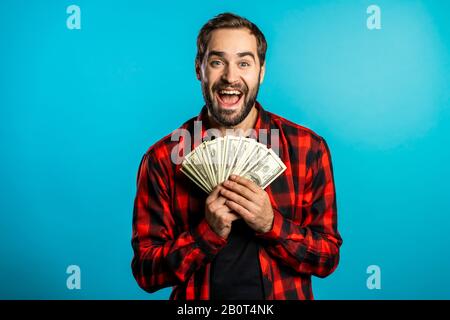 L'uomo entusiasta soddisfatto che mostra il denaro - banconote in dollari USA su blu Foto Stock