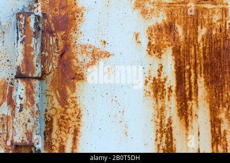 Particolare di una porta arrugginita su cerniere arrugginite.Rust sfondo con graffi e resti di vernice blu. Foto Stock