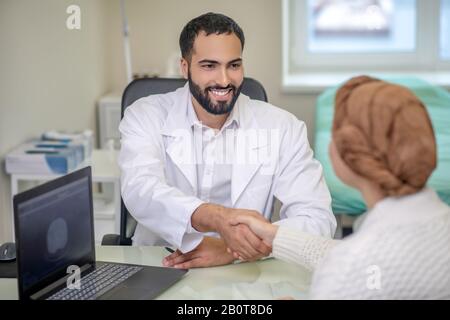 Il medico maschile dai capelli scuri che tiene le mani delle sue pazienti femminili Foto Stock