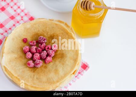 Frittelle appena sfornate con lamponi e miele su un piatto. Dolci tradizionali fatti in casa. Maslenitsa. Foto Stock