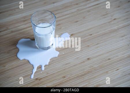 vista dall'alto, primo piano di vetro in una pozza di latte versato su un tavolo di legno marrone chiaro con illuminazione naturale Foto Stock