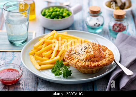 Torta di carne con patatine fritte su un piatto bianco. Sfondo in legno. Primo piano. Foto Stock