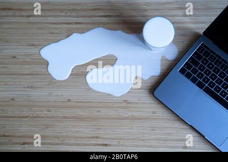 vista dall'alto sul coperchio del bicchiere di latte versato su uno sfondo in legno della scrivania vicino al computer portatile copyspace disponibile Foto Stock