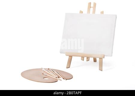 Piccolo treppiede con cornice in tela, tavolozza di legno e nuove spazzole isolate su bianco con percorso di lavoro. Foto Stock