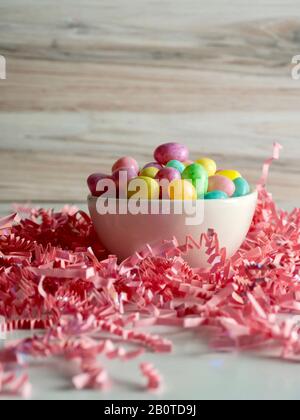 Ciotola di gelatina fagioli pastello colorato su un letto di carta rosa triturato increspato su con uno sfondo di legno per Pasqua Foto Stock