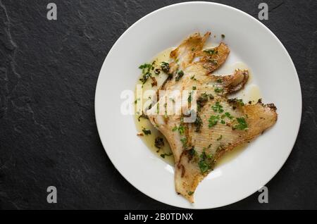 Un'ala di raggio da un raggio del torace, Raja clavata, che è stata cucinata in un modo tradizionale. È stato fritto in una padella di rame con olio d'oliva, burro Foto Stock