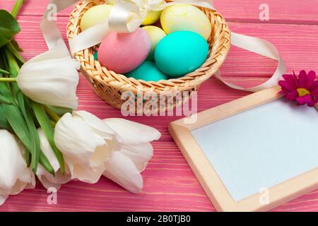 uova colorate e fiori di tulipano sullo sfondo di tavole di legno Foto Stock