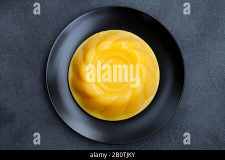 Budino di mango, gelatina, dessert su piatto nero. Sfondo grigio pietra. Vista dall'alto. Foto Stock