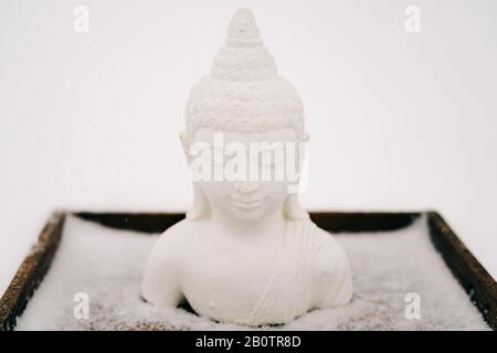 Figurina bianca del Buddha fatta di intonaco su uno stand di legno durante una nevicata Foto Stock