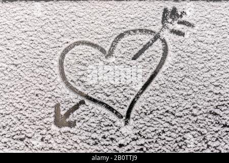 un cuore e una freccia di un arco che lo perfora, una silhouette ravvicinata sulla neve, disegnato sul vetro con un dito. Immagine romantica, separazione d'amore un Foto Stock